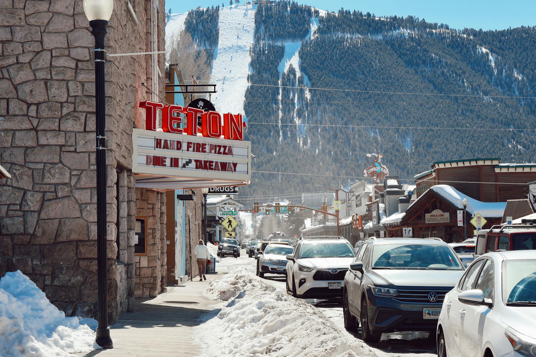 Scenic view of downtown Jackson, WY featuring cars, a snowy street, and Teton mountains.